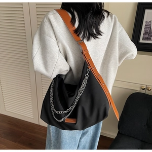 Detail of a black large-capacity nylon tote bag with silver chain and brown leather strap