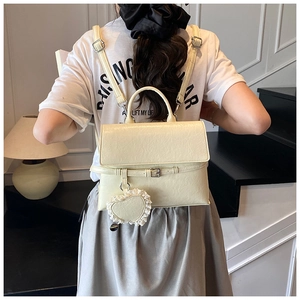 Detail showing the creamy white faux leather texture and heart lace charm of the backpack