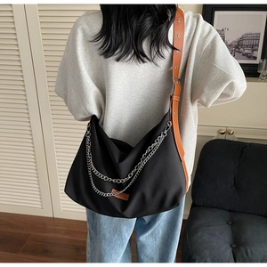 Detail of black nylon crossbody bag with double silver chains and orange leather strap