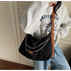 Détail du sac en nylon noir avec chaîne argentée et bandoulière marron sur modèle