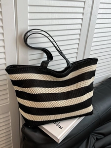 Minimalist black and white striped tote bag with leather straps on a sofa