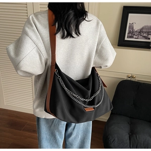 Detail of black canvas dumpling bag featuring silver chains and brown leather strap