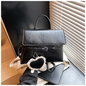 Detail of a black textured faux leather backpack with a lace heart charm and buckle strap