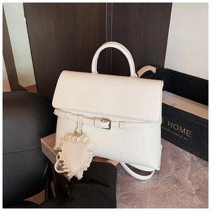 Close-up of a white textured leather backpack featuring a heart lace charm and silver buckle