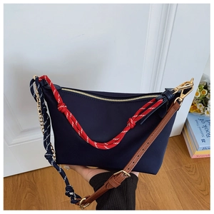 Detail of navy canvas crossbody bag featuring red woven handles and leather strap