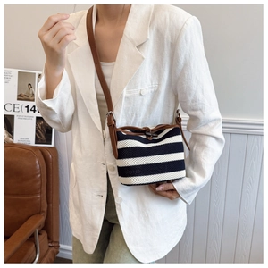 Detail of hand-woven black and white striped bucket bag with brown leather shoulder strap