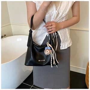 Close-up of black lychee-textured underarm bag with cute monkey plush charm and silver hardware
