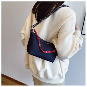 Detail of dark blue nylon handbag featuring woven rope handles and a gold chain strap