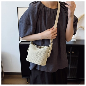 Close-up of beige woven bucket bag with dark horn buckle closure worn by a model
