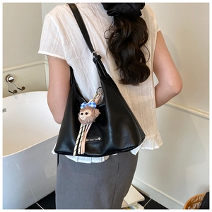 Detail of black faux leather hobo shoulder bag with plush charm and silver logo plate