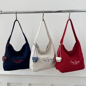 Three canvas tote bags in navy, cream, and red with stylish lettering and small charms