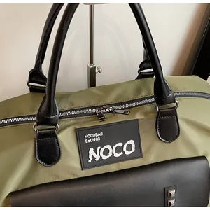 Close-up of green travel bag with black leather handles and silver metal hardware details