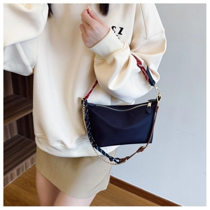 Detail of black nylon shoulder bag with colorful woven strap and gold chain detail