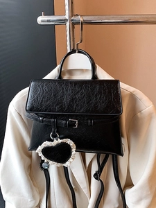 Black pleated PU leather backpack with heart charm hanging on a cream blazer