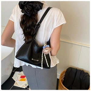 Detail of black crescent shoulder bag with metallic logo and plush bear pendant