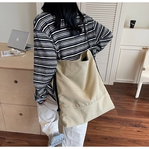 Close-up of a large khaki canvas bucket bag featuring a wide black shoulder strap