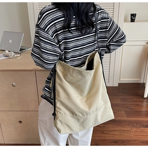 Detail shot of a large beige canvas tote bag with black straps worn in an office setting