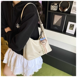 Detail of a creamy white hobo bag with a cute bear plush pendant in a stylish interior
