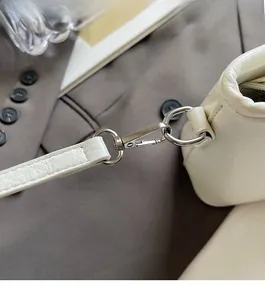Detail of silver metallic lobster clasp and glossy beige leather on the bucket bag