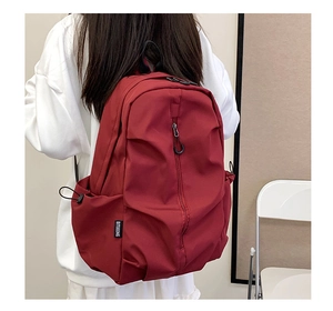 Detail view of deep red durable nylon backpack with side drawstring pocket and branding