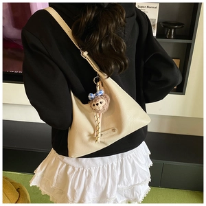 Detailed view of cream crescent underarm bag featuring a cute plush bear charm and leather logo