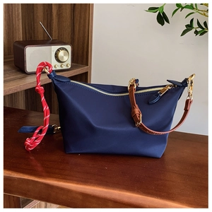 Detail of navy blue nylon crossbody bag with golden zipper and red braided rope charm