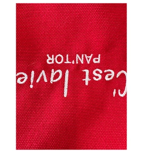 Close-up of red canvas tote bag with white C'est la vie embroidery and fine fabric texture