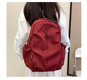 Detail view of the deep red nylon backpack featuring side pockets and a branded woven label