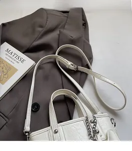 Detail of off-white pleated leather bag with silver chain on a brown blazer background