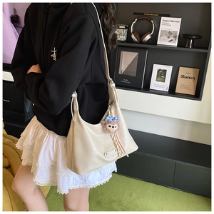 Detail of off-white pleated shoulder bag with cute plush bear charm in a cozy indoor setting
