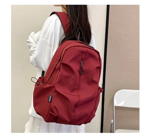 Detail view of deep red nylon backpack featuring side pockets and padded shoulder straps