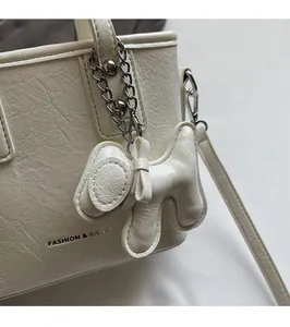 Close-up of off-white leather bucket bag with dog-shaped charm and pleated texture