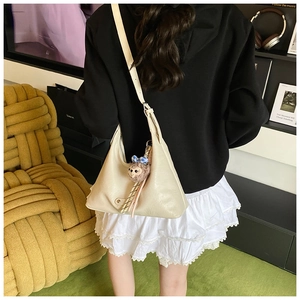 Close-up of cream leather shoulder bag featuring a cute plush animal charm with blue bow