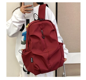 Detail of burgundy nylon backpack featuring a vertical zipper and black brand logo label