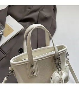Close-up of a white textured leather bucket bag featuring a delicate metal bow charm