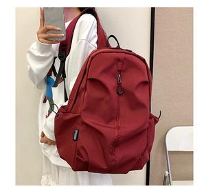 Detail view of burgundy backpack side pocket and woven label worn by a person