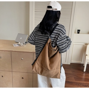 Brown canvas bucket bag with wide black strap shown in a minimalist office setting