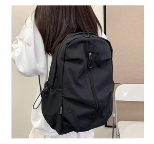 Detail of lightweight black nylon backpack showing side drawstring pocket and fabric texture