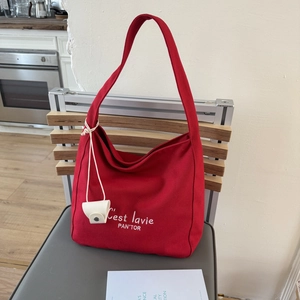 Detail of red canvas hobo bag with white typography and small card holder on a chair