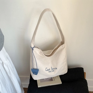 Close-up of minimalist canvas tote bag with blue embroidery and leather charm detail