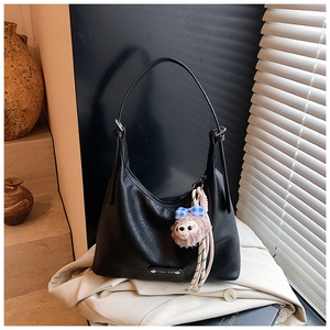 Detail of black pebbled leather hobo bag with a pink plush charm and silver logo plate