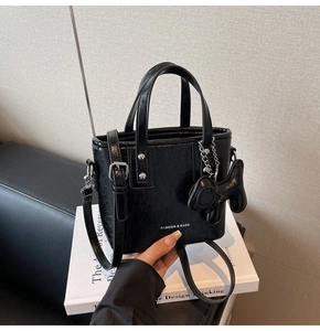 Détail du sac seau noir en cuir verni avec texte blanc et charmant pendentif chien