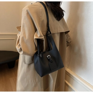 Détail du sac seau noir en cuir grainé avec boucle argentée sur un trench-coat beige