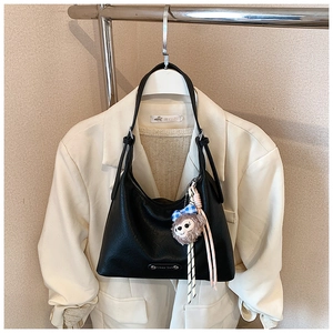 Detail of black leather crescent underarm bag with cute plush bear pendant accessory