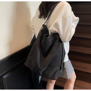 Detail view of large black canvas bucket bag shown on shoulder in indoor staircase setting