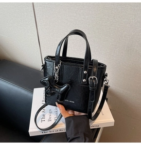 Détail du sac bandoulière noir avec rivets et breloque chien posé sur un livre