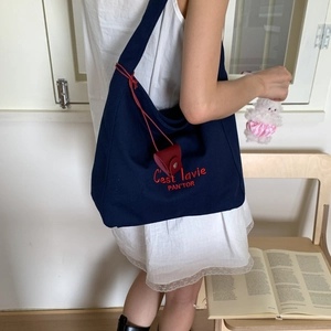 Detail of navy canvas tote bag featuring red embroidery and a cute white plush charm