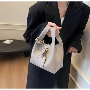 Détail d'un sac seau minimaliste en cuir grainé beige tenu par un mannequin à la main
