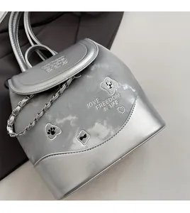 Detail of silver metallic backpack featuring chain handle and 'Love Freedom' embroidery
