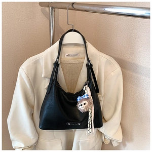 Detail of black lychee grain leather underarm bag with cute plush pendant and metal logo